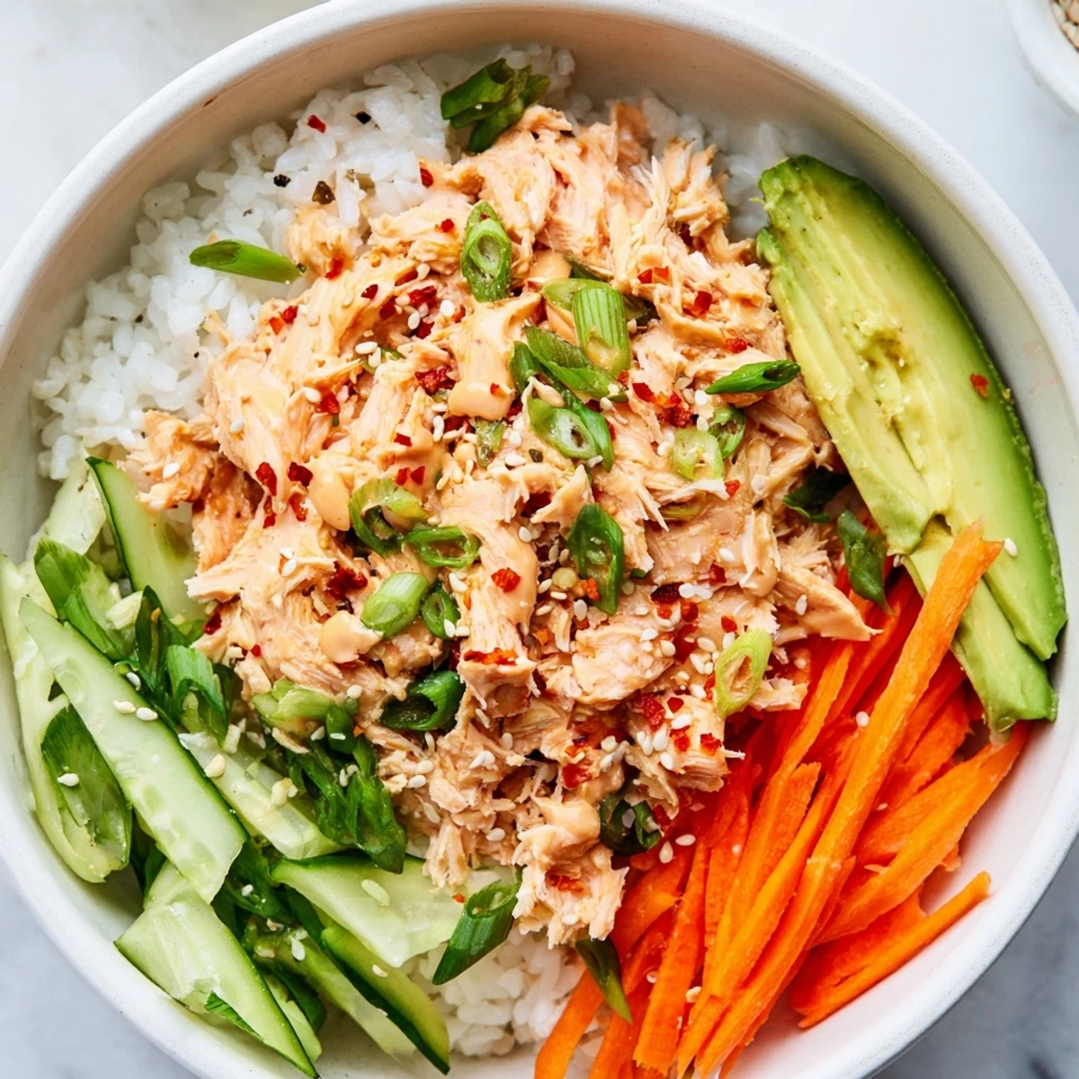A close-up of a Spicy Canned Salmon Rice Bowl featuring flaky salmon and fresh cucumber.