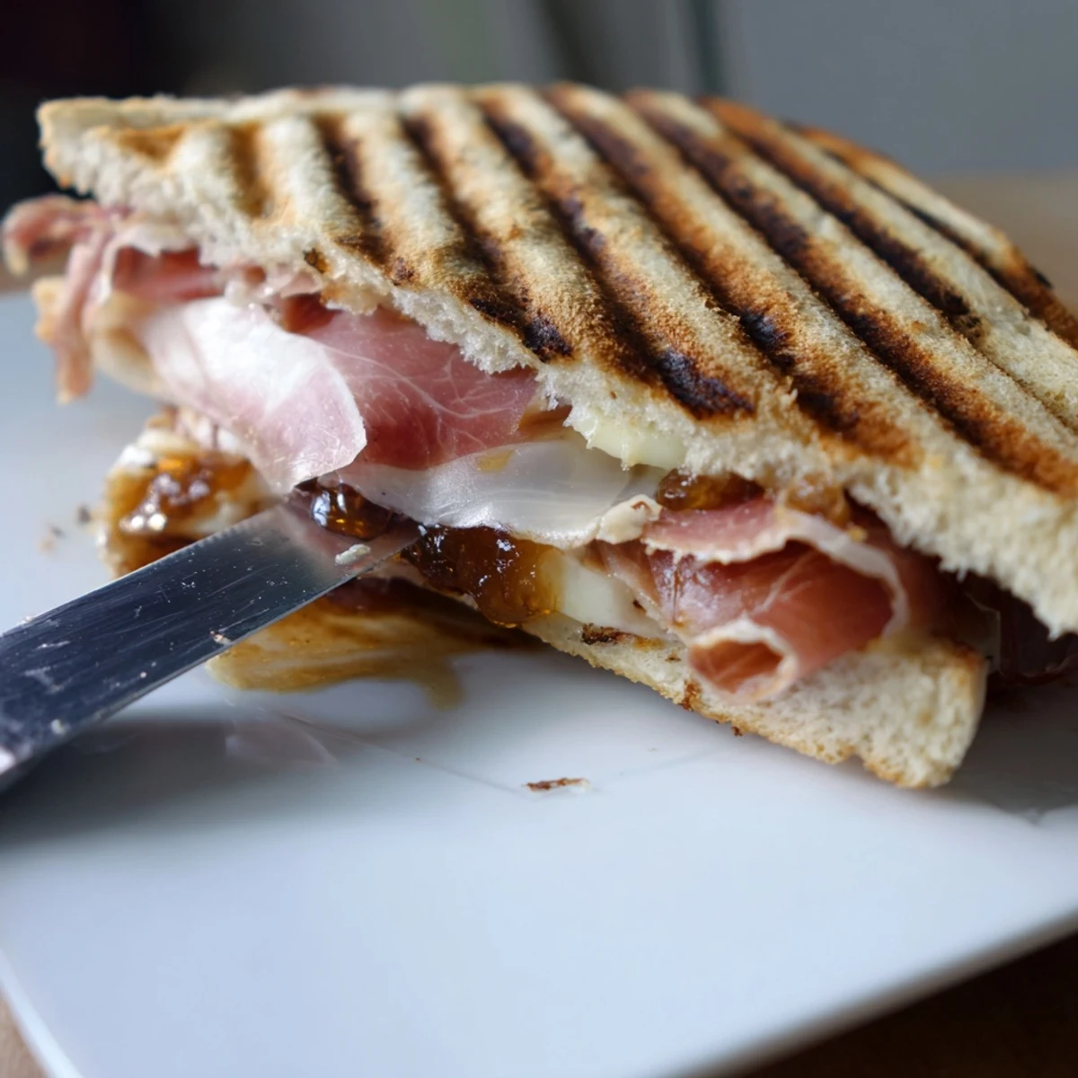 Golden-brown Crispy Prosciutto & Fig Panini on a rustic wooden board, showcasing melted cheese and savory meat.