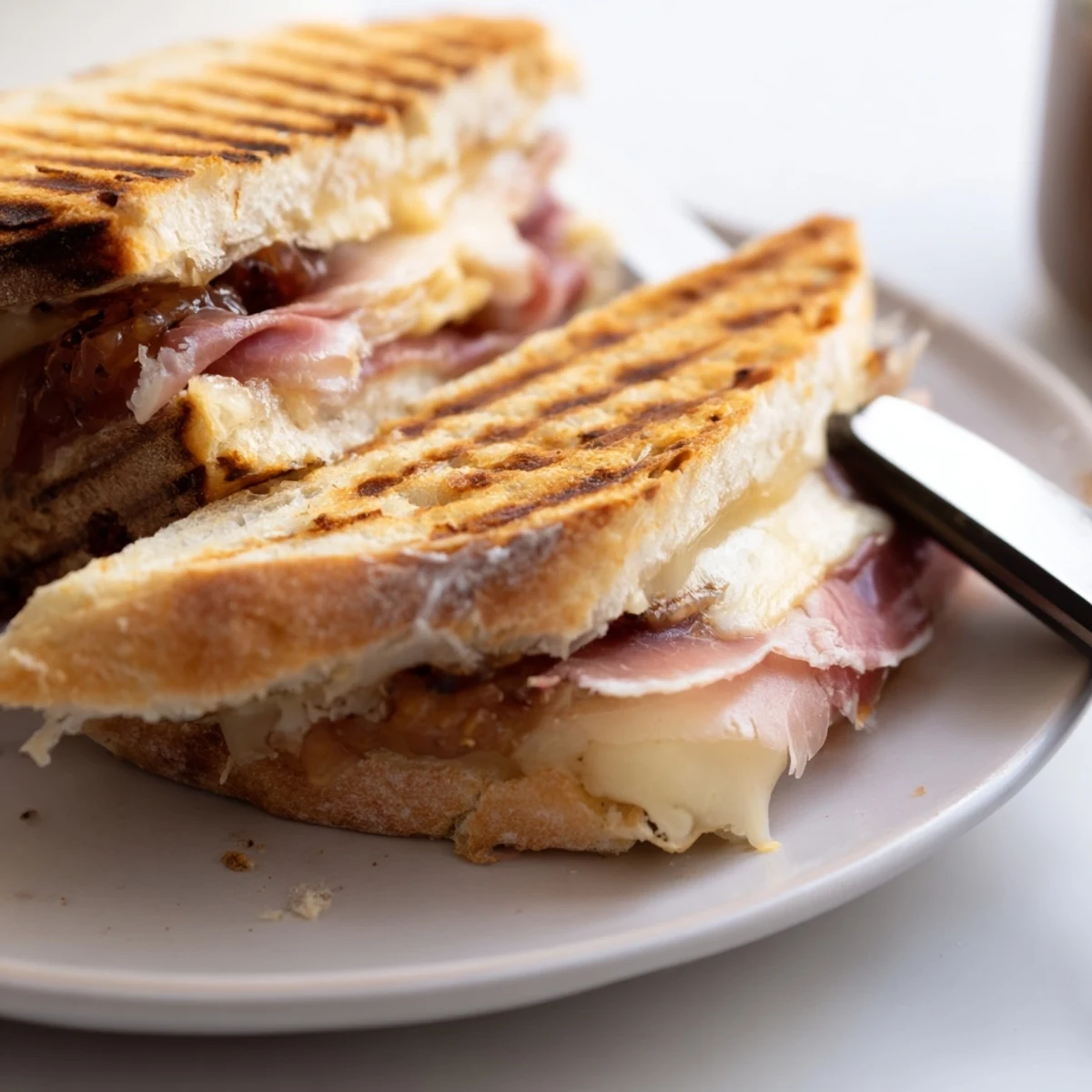 Freshly sliced Crispy Prosciutto & Fig Panini revealing layers of fig jam and gooey fontina on a plate.