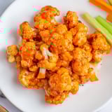 Close-up of crispy, spicy Buffalo Cauliflower Bites coated in tangy sauce, a perfect party appetizer.