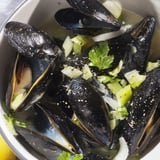 A photo showcasing a steaming pot of Belgian Moules Marinière with aromatic white wine and savory broth.