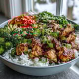 Colorful Chicken and Rice Bowl garnished with sliced green onions and sesame seeds, displayed on a rustic wooden table.