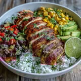 Ready-to-eat Cajun Chicken Bowl featuring juicy chicken, fluffy rice, corn, and black beans, garnished with fresh cilantro and avocado slices, with lime wedges on the side.