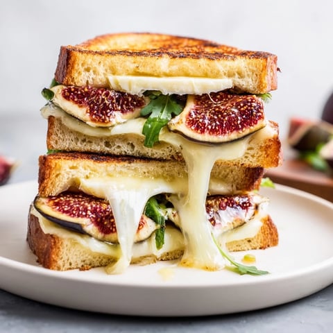 Picture of golden, melty Fig, Brie & Arugula Grilled Cheese, oozing delicious Brie and fig.