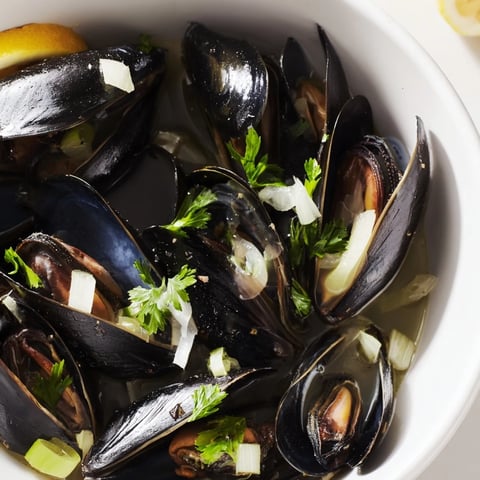 Steaming Belgian Moules Marinière with fresh herbs and plump mussels, ready to serve with crusty bread.