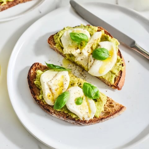 A close-up of the Avocado Mozzarella Tartine, featuring golden toasted sourdough topped with creamy smashed avocado and melted mozzarella, garnished with fresh basil and red pepper flakes.