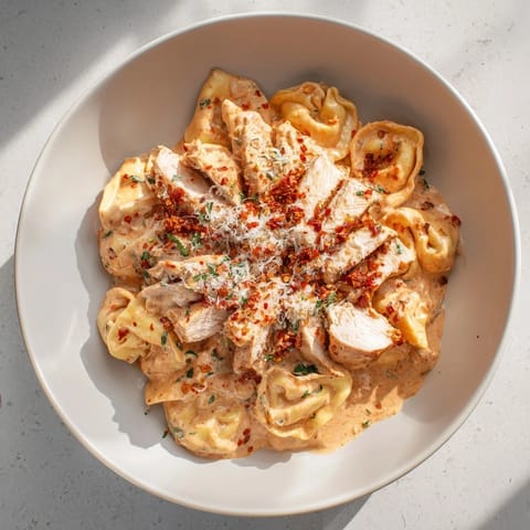 A skillet of golden-brown Marry Me Chicken Tortellini with sun-dried tomatoes and Parmesan cheese.