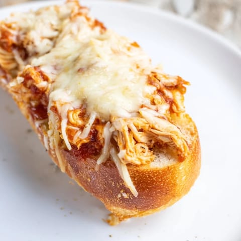 A close-up of Chicken Parm Stuffed Garlic Bread, revealing tender chicken and marinara sauce inside a crispy garlic butter baguette.  