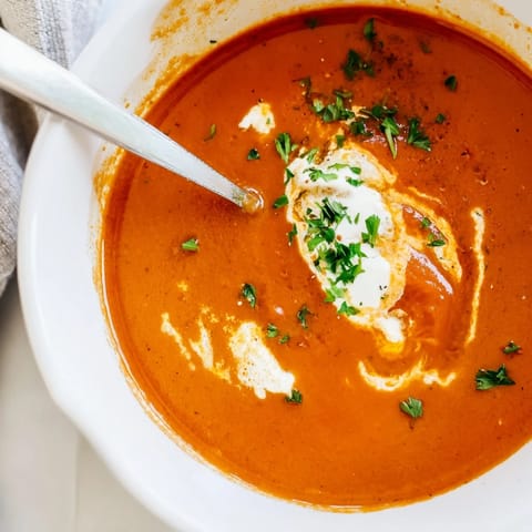 A pot of silky roasted red pepper soup simmering with caramelized onions, carrots, and celery for deep, comforting flavor.  