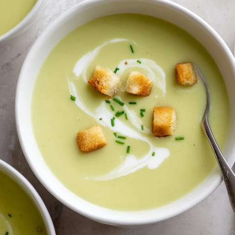 A bowl of creamy broccoli soup garnished with chives and a swirl of cream, served alongside crusty bread.  